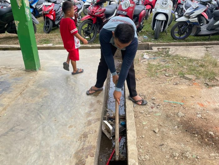 Pegawai Tata Usaha Bersihkan Selokan Madrasah Pagi Ini